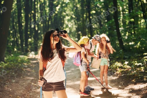 Preview: Girl standing in front of her friends. Kids strolling in the forest with travel equipment