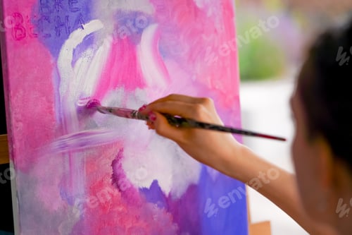 Preview: Close-up of a girl artist with a brush applying oil paint to a painting standing on easel