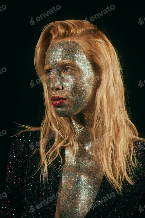 Preview: portrait of blonde woman with green eyes and glitter on face and body posing on black backdrop
