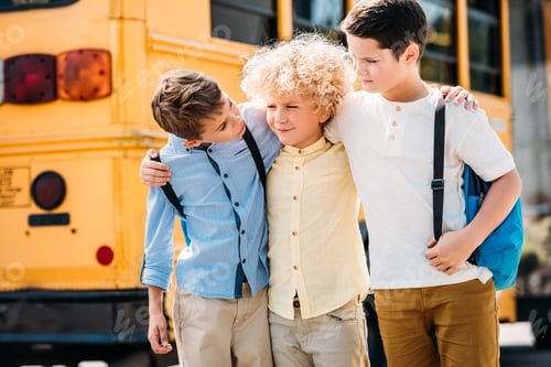 Preview: happy little schoolboys embracing and talking in front of school bus