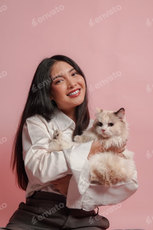 Preview: Pretty young Asian woman in white shirt is holding a white ragdoll cat and smiling to the camera.