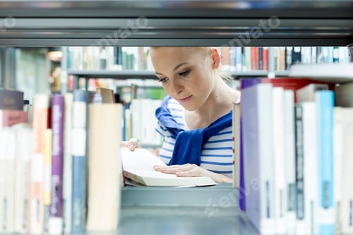 Preview: Student in a university library reading book at shelf