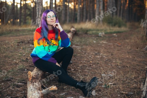 Preview: Young woman hipster with purple hair wearing glasses and colorful sweater in an autumn forest.