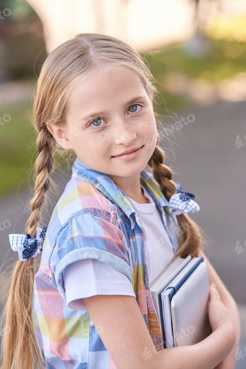 Preview: Young caucasian female child with braided hair holding books outdoors in casual