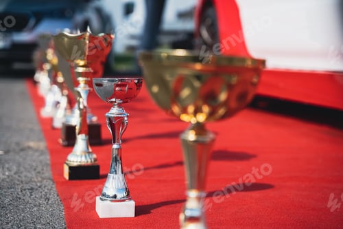 Preview: close up perspective view of golden and silver trophy on red carpet with cars in the background