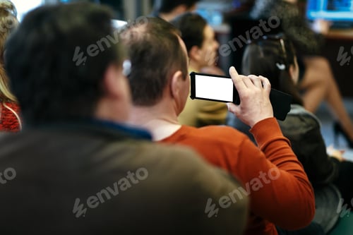 Preview: stylish man holding phone with empty white screen in audience