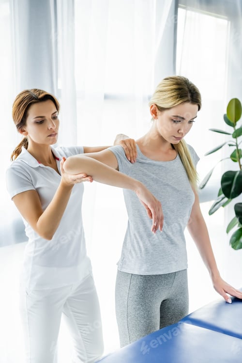 Preview: chiropractor touching shoulders of attractive patient in grey t-shirt