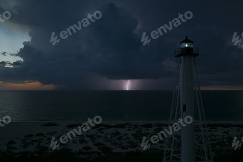Preview: White tall lighthouse on sea shore with blinking light at stormy night for commercial vessels