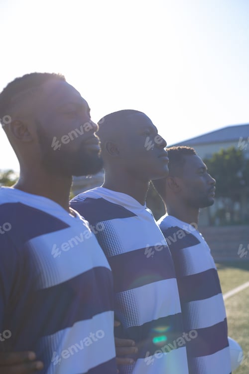 Preview: Three African American young male athletes wearing striped sportswear are standing together on field