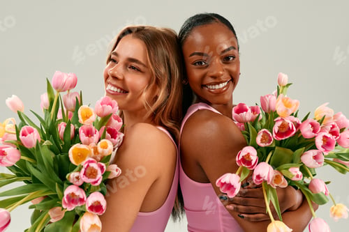 Preview: Two smiling women holding tulip bouquets in pink tops and jeans on white background