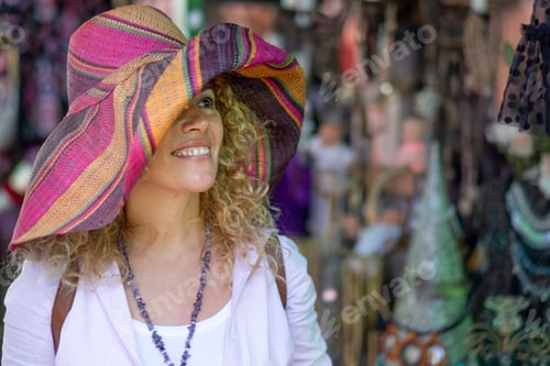 Preview: Attractive smiling woman blonde and curly haired enjoying the flea market with a beautiful Hat