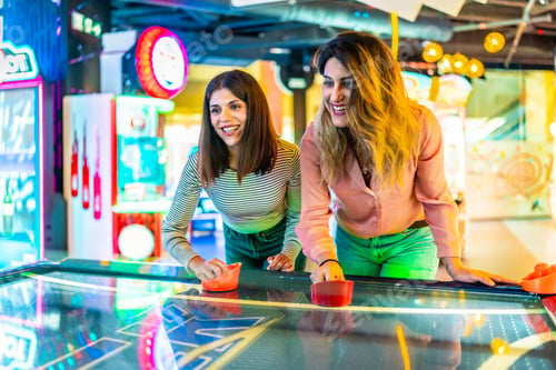 Preview: Two happy friends playing air hockey in a colorful arcade