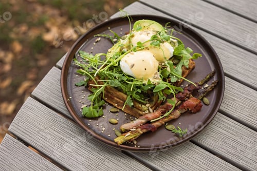 Preview: Eggs Benedict with Hollandaise Sauce on waffles with avocado, arugula, green asparagus and bacon
