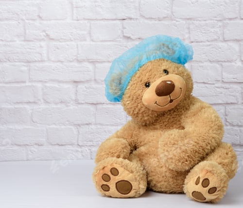 Preview: Brown teddy bear sits in protective medical disposable blue cap