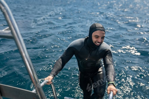 Preview: Smiling diver climbing boat ladder after scuba diving in ocean