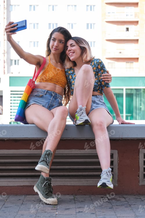 Preview: Young lesbian couple smiling and taking a selfie outdoors.