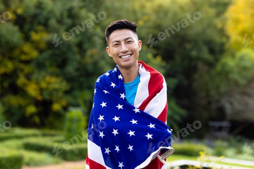 Preview: Portrait of happy asian man covered with flag of usa in garden