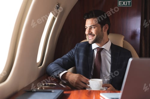 Preview: smiling businessman holding cup of coffee in plane during business trip