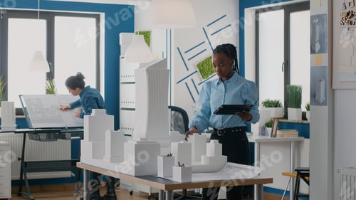 Preview: Architect using digital tablet to design layout of building model and maquette in office