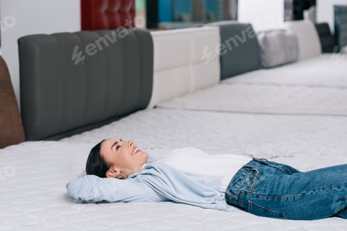 Preview: side view of smiling customer lying on orthopedic mattress in furniture store