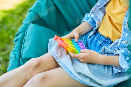 Preview: A little girl the on hanging chair outdoors play pop it, kid hands playing with colorful pop It