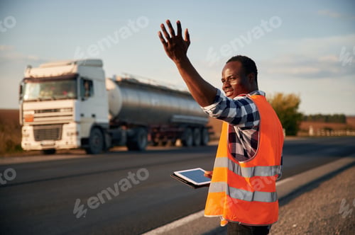 Preview: Showing the way. Black man is standing on the road with truck on it