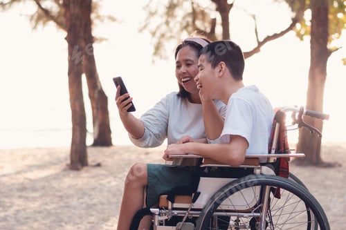 Preview: Disabled child on wheelchair and parent having fun using mobile phone.