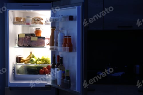 Preview: Open refrigerator full of products in kitchen at night