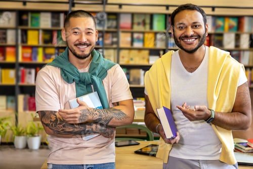 Preview: In library. Students standing with books in library