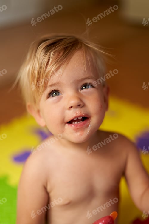 Preview: Laughing little kid with dirty face and ice cream in hand sits on the floor
