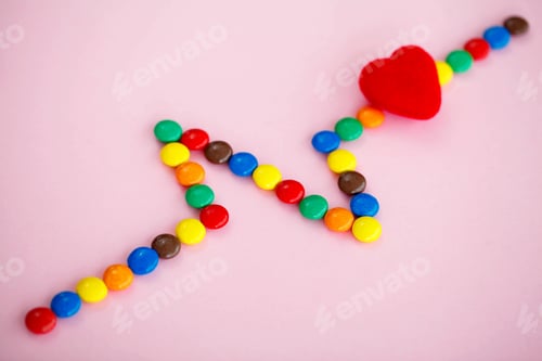 Preview: Colored Candy in the Form of Cardiogram on the Pink Background.