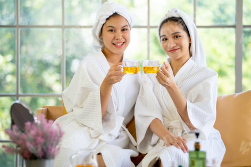 Preview: Two Asian beautiful girl hold cup of tea and look to camera after massage or spa