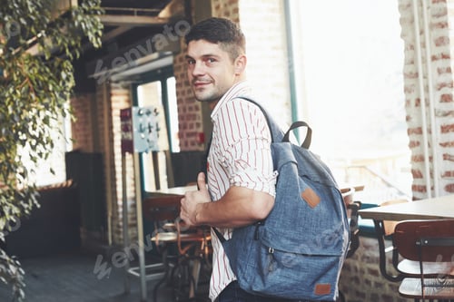 Preview: Looking behind. Man in casual clothes and backpack stands indoors