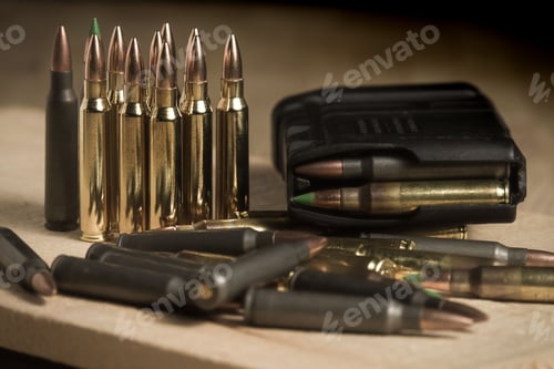 Preview: 223 caliber (5.56mm) bullets standing or laying next to a full AR-15 magazine full of ammo