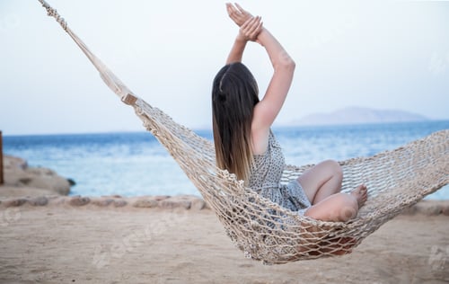 Preview: A young woman sits in a hammock by the sea and relaxes.