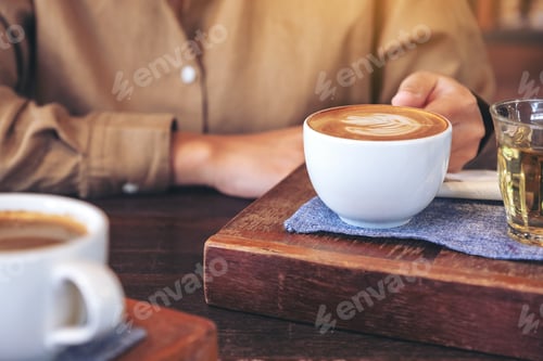 Preview: Closeup image of woman's hands holding a cup of hot coffee on wooden table