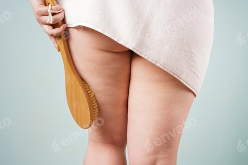 Preview: A young plus size woman in a towel holds a natural dry massage brush.