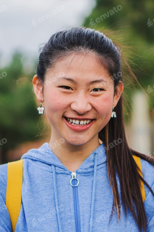 Preview: Vertical close up portrait of cute asian schoolgirl standing and laughing at campus. Young chinese
