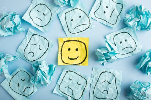 Preview: A sad face watching smiling faces from afar. Happy and sad faces drawn on blue stickers.