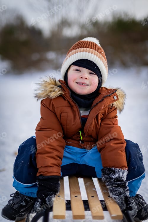 Preview: Cheerful child rides a sled during a winter walk