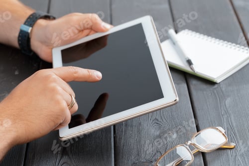 Preview: hands of a man holding tablet device over a wooden workspace table