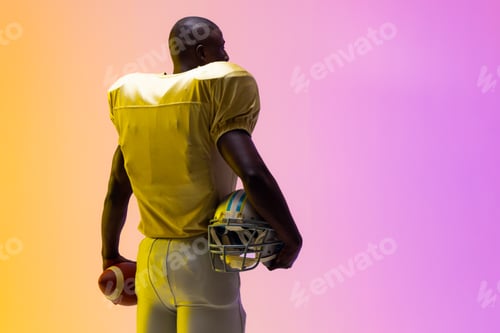 Preview: African american male american football player holding ball with neon yellow and purple lighting