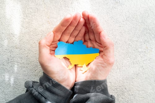 Hands holding the national flag of Ukraine in the shape of the borders of Ukraine
