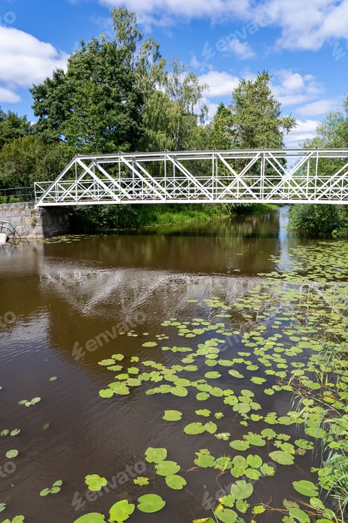Preview: White iron bridge over a tranquil river surrounded by lush greenery in Uppsala, Sweden