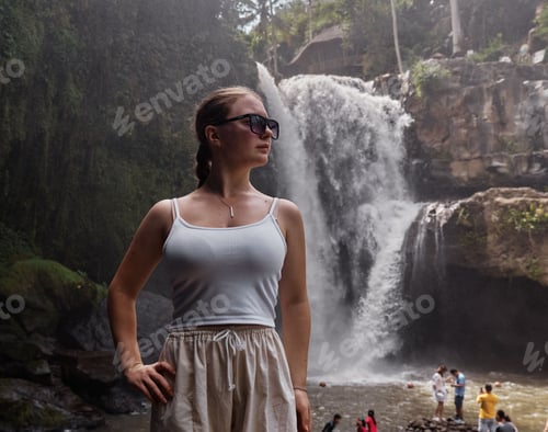 Preview: Caucasian woman with sunglasses posing with the beautiful waterfall in the background