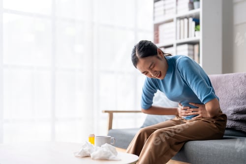 Preview: A woman is sitting on a couch with a stomach ache