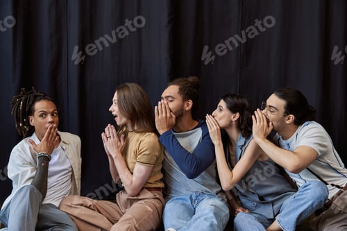 Preview: multiethnic colleagues sitting and telling gossip to astonished colleague in coworking office