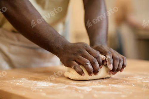 Preview: Close up of young Black man kneading dough making fresh bread in artisan bakery