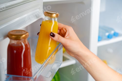 Preview: Female hand taking orange juice jar from a fridge