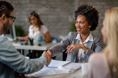 Preview: Black happy financial advisor shaking hands with clients in the office.